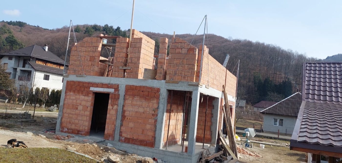Casă la roșu cu forma acoperișului conturată, pe fundal de deal împădurit, Maramureș