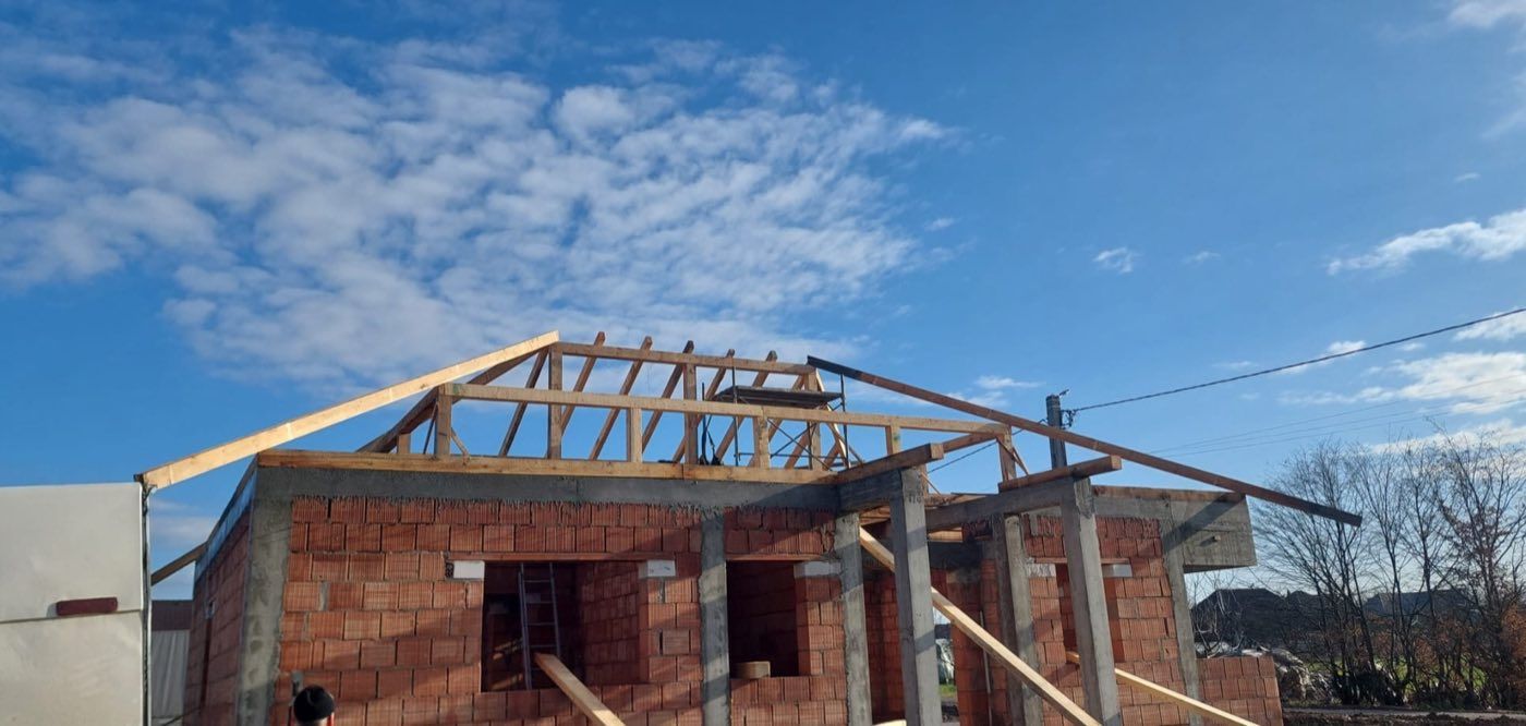 Structură de șarpantă din lemn, văzută de jos, pe cer înnorat