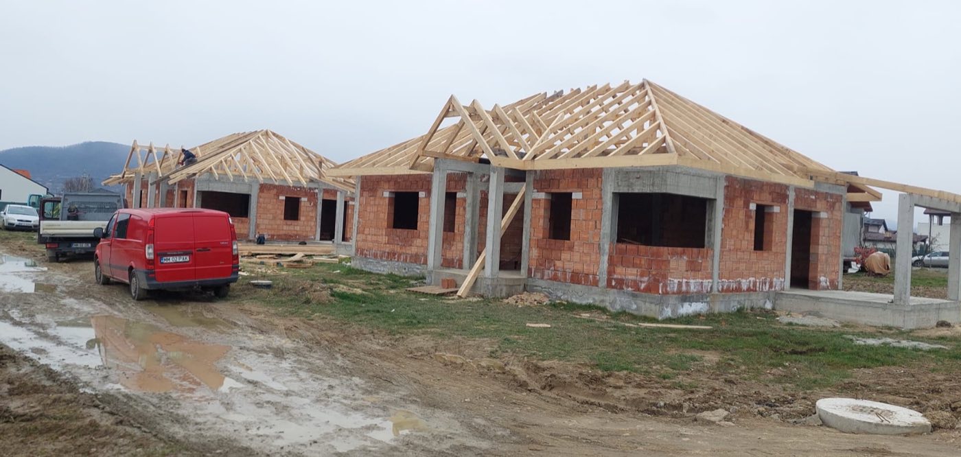 Două case cu șarpantă montată, drum noroios și dubă roșie în prim-plan