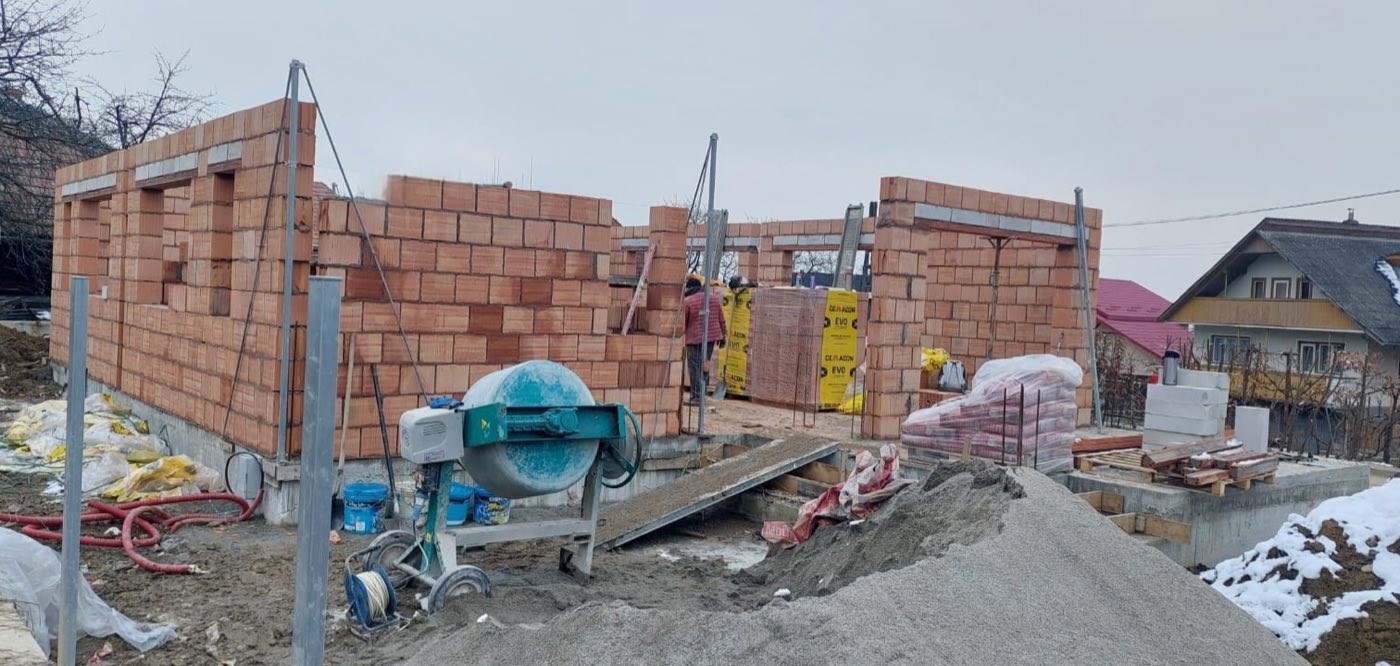 Ziduri de cărămidă la roșu, cu muncitori și betonieră, iarna