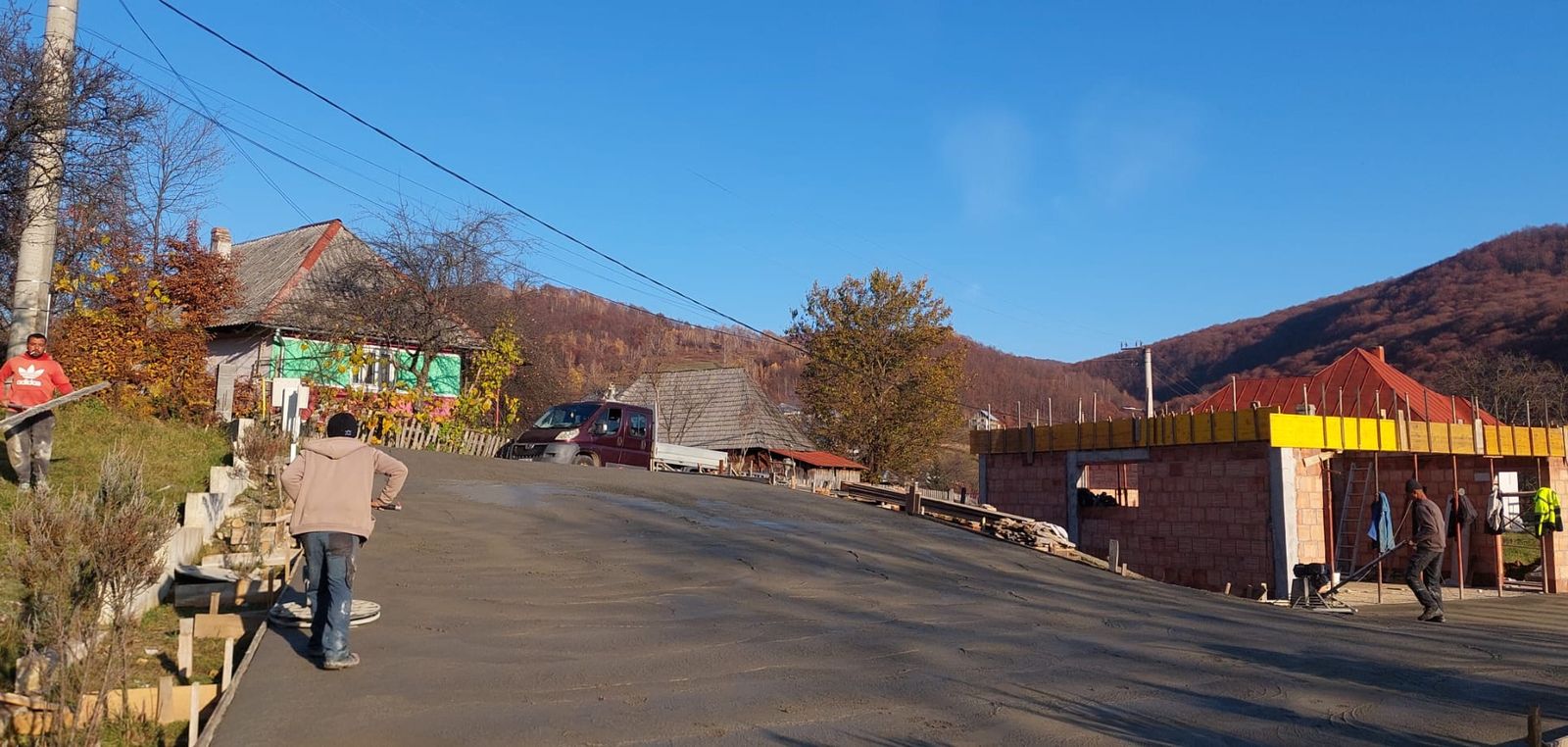 Turnare beton într-o curte de sat, cu casă tradițională pictată și construcție nouă alăturată, Maramureș